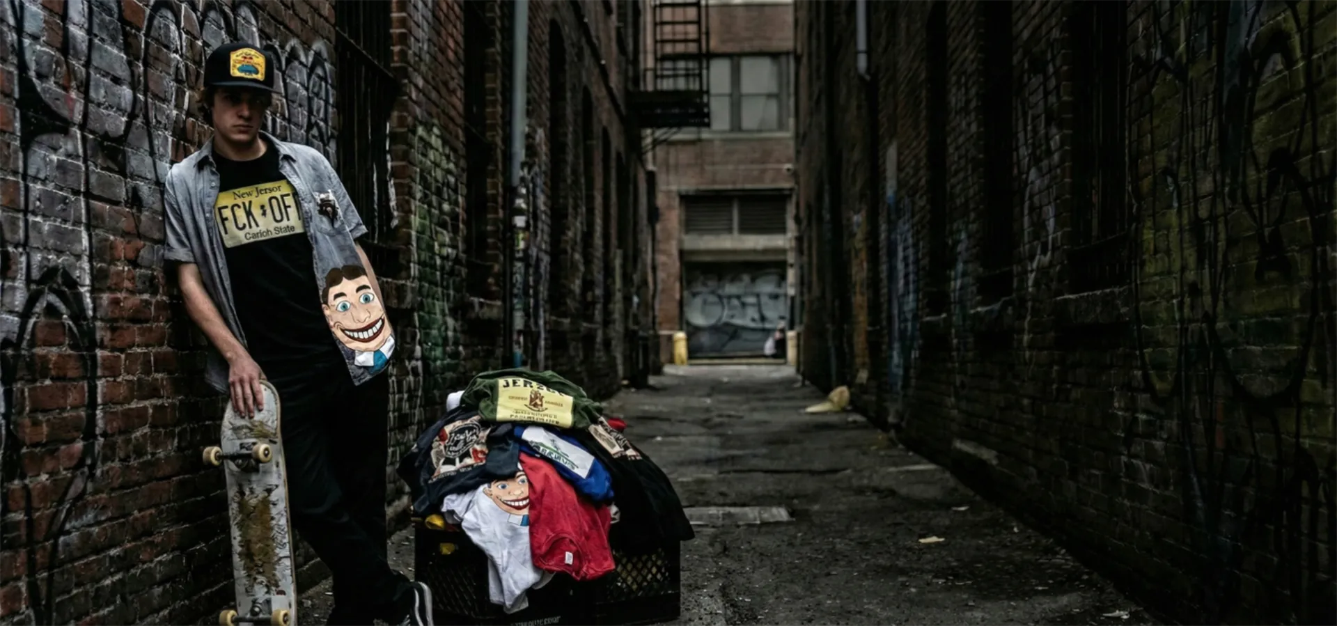 Person holding a skateboard in an alleyway with graffiti on the walls.